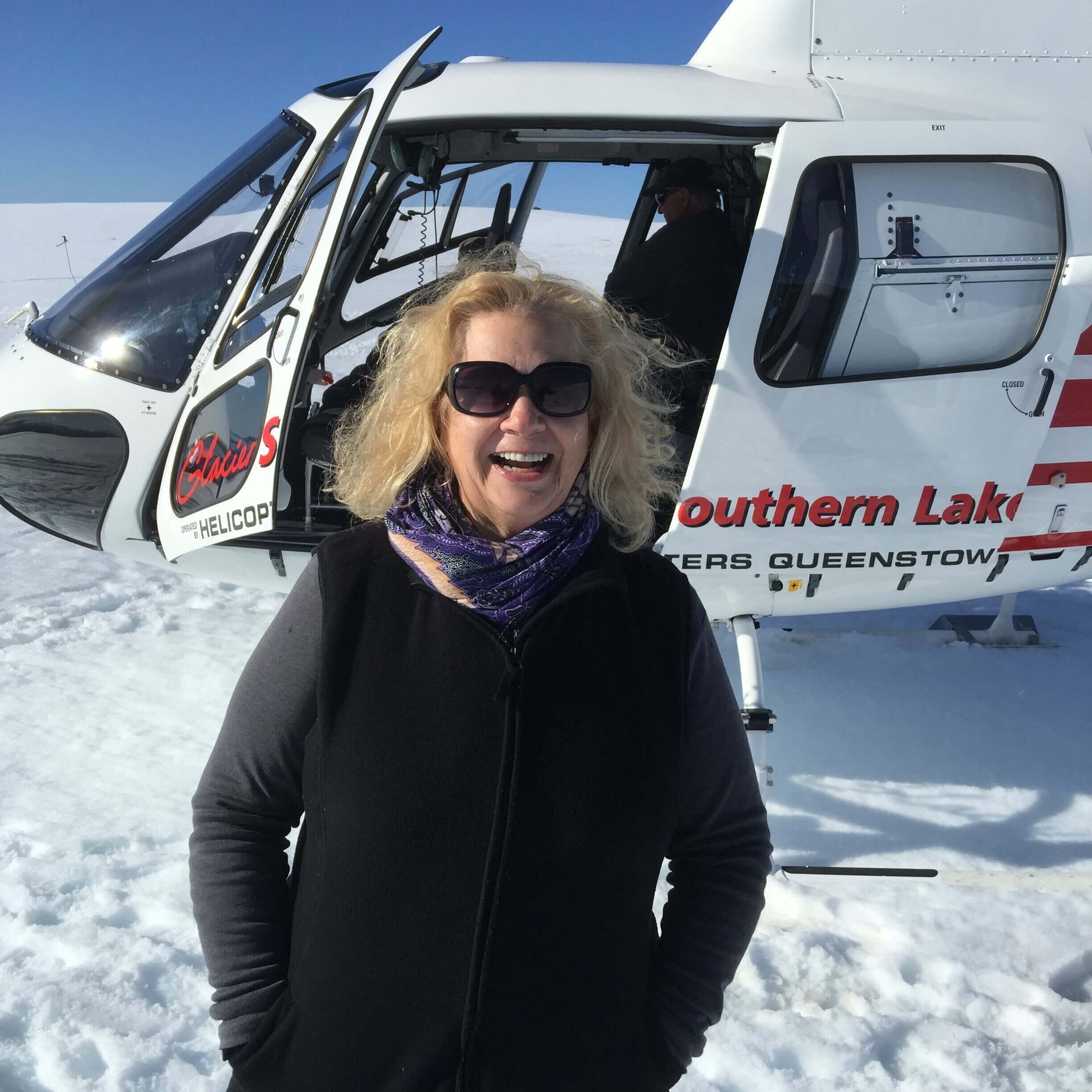Smiling woman in sunglasses by helicopter on snow